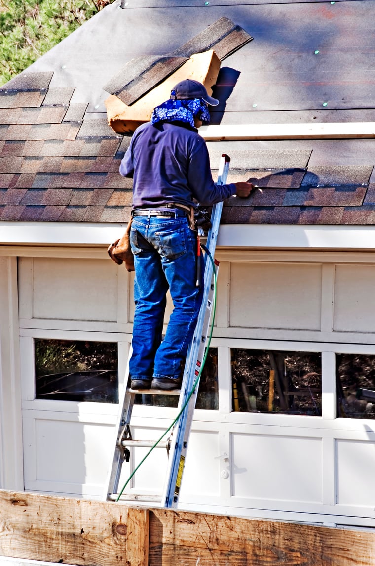 man standing on a ladder working on a damaged roof